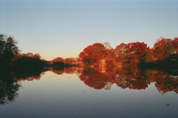 A scenic autumn landscape in New England, with vibrant red and orange trees reflecting in a calm lake.