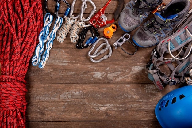 A detailed flat lay of essential climbing gear including ropes, carabiners, a harness, climbing shoes, and a helmet, neatly arranged on a natural rock surface.