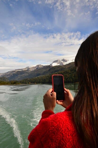 A person holding a smartphone displaying a travel booking confirmation, with a scenic view of mountains and a lake in the background, signifying successful redemption for a desirable location.