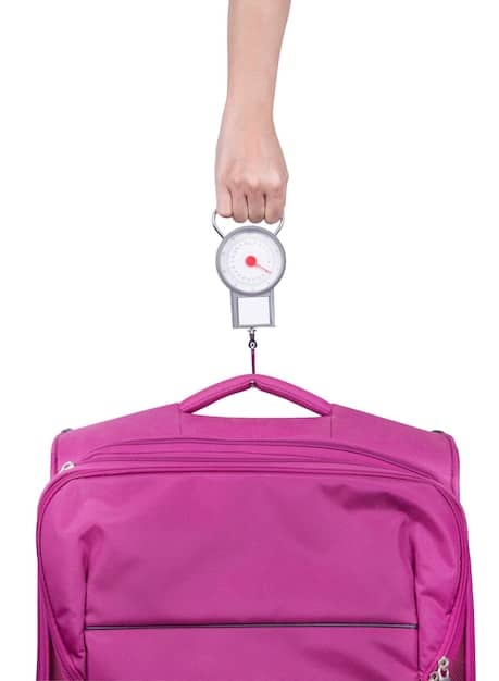A person meticulously weighing their suitcase on a bathroom scale, looking determined.