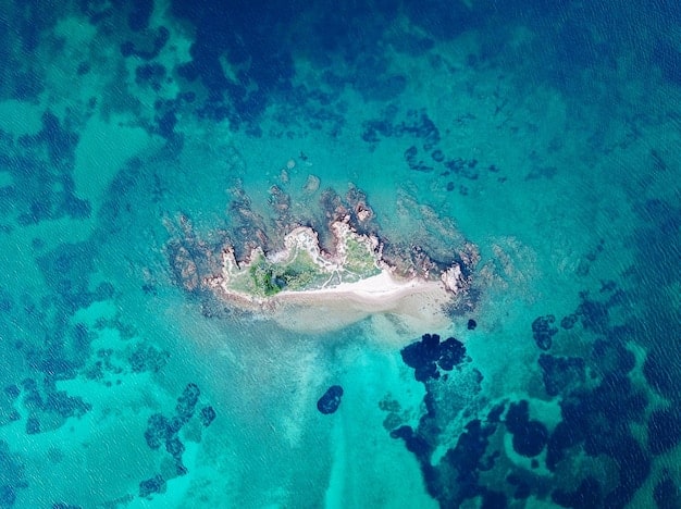A vibrant aerial view of Anacapa Island in Channel Islands National Park, showcasing its dramatic sea cliffs, arch formations, and the clear blue Pacific Ocean, with kayakers navigating below.