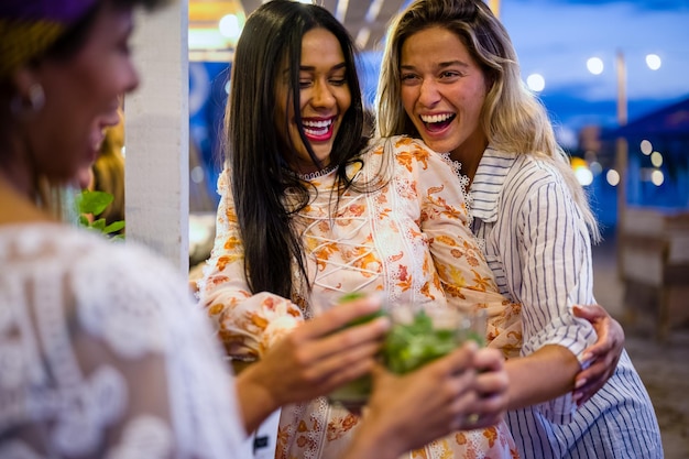 A group of friends laughing as they enjoy a meal at a vibrant food market in a US city. The photo captures a variety of ethnic foods from different stalls, with each person holding a different dish. The overall atmosphere is lively and cheerful, with bright lighting and colorful decorations.