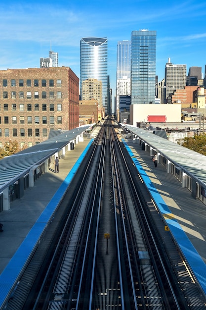 A daytime shot of a Chicago 'L' train traveling above the city streets. The train is brightly lit and carries a mix of passengers. The surrounding architecture includes classic Chicago buildings and busy streets below filled with cars and pedestrians, illustrating the integration of the elevated train system into the city's daily life.