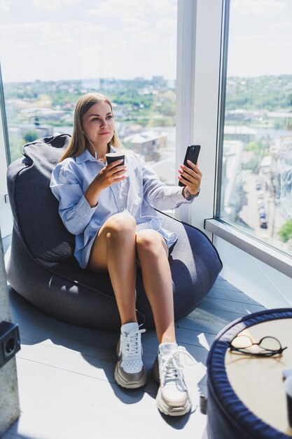 A traveler relaxing in an airport lounge, enjoying complimentary refreshments and Wi-Fi, with a view of airplanes taking off on the runway. The scene represents the premium benefits and travel experiences gained through airline loyalty programs.