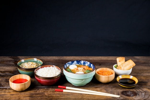 A table setting with various international dishes. Chopsticks are placed neatly next to a bowl of noodles, while a knife and fork are arranged beside a plate of steak. It highlights diverse global dining etiquette.