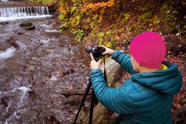 A photographer adjusting settings on a professional camera with a wide-angle lens, overlooking a vibrant fall landscape in the Great Smoky Mountains, emphasizing technical precision.