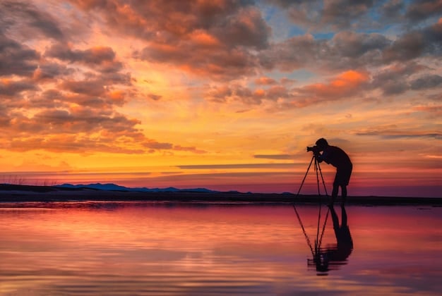 A photographer adjusting their tripod-mounted camera with a wide-angle lens, overlooking Horseshoe Bend at sunset, capturing the dramatic curves of the Colorado River.