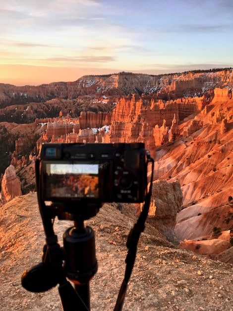 A detailed shot of a camera on a tripod, with a wide-angle lens attached, pointing towards a vibrant sunset over the Grand Canyon, emphasizing the camera's features and the dramatic landscape.